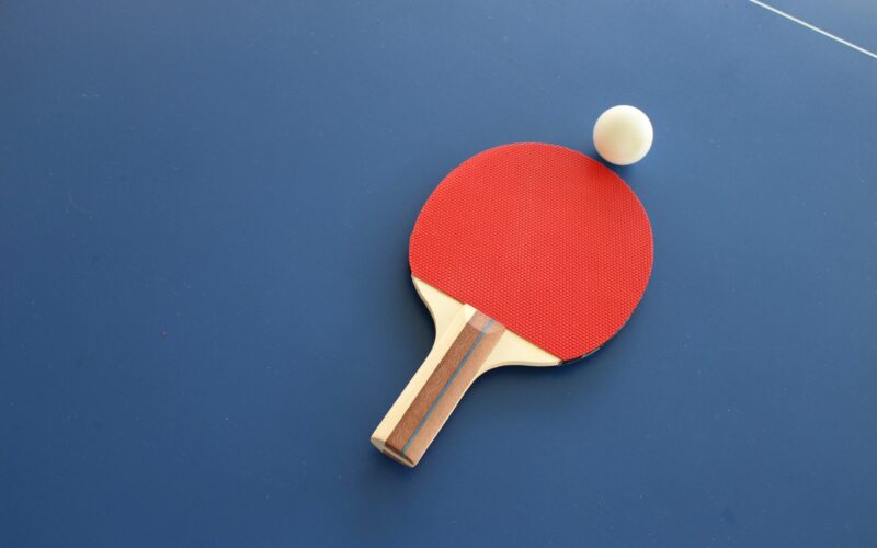 Närbild på ett pingisracket och en pingisboll mot ett blått pingisbord.
