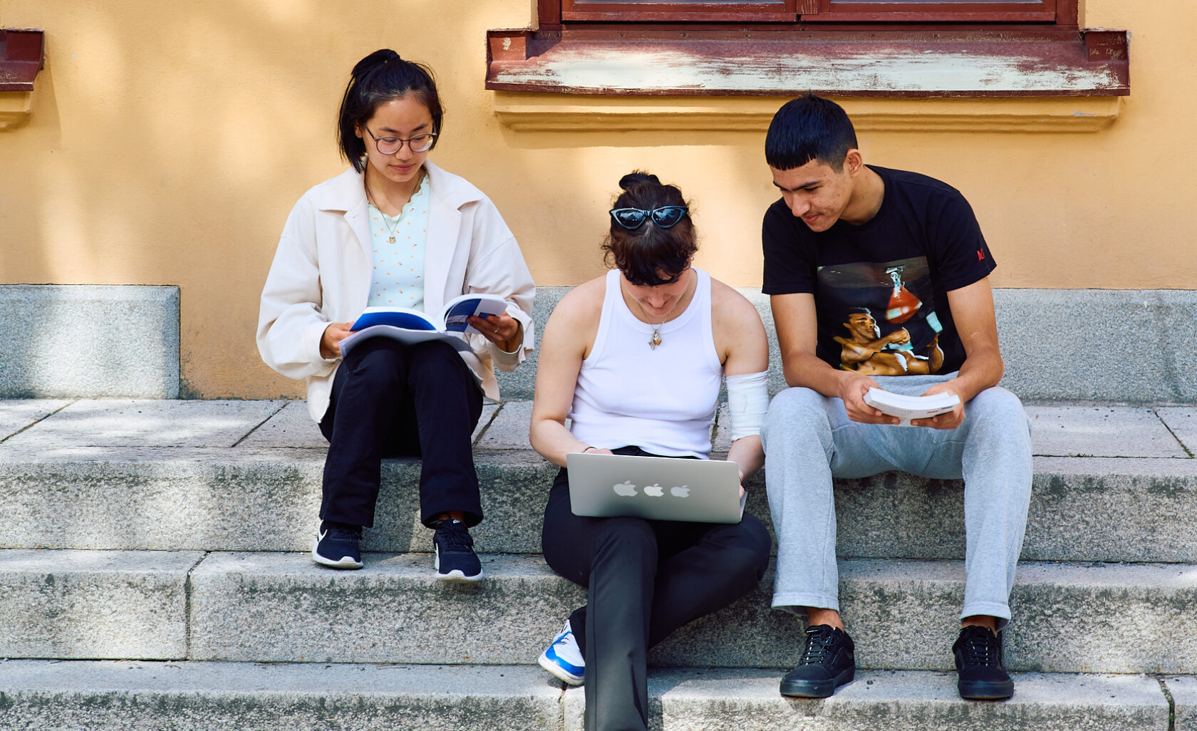 Tre elever sitter på en trappa utomhus och studerar.
