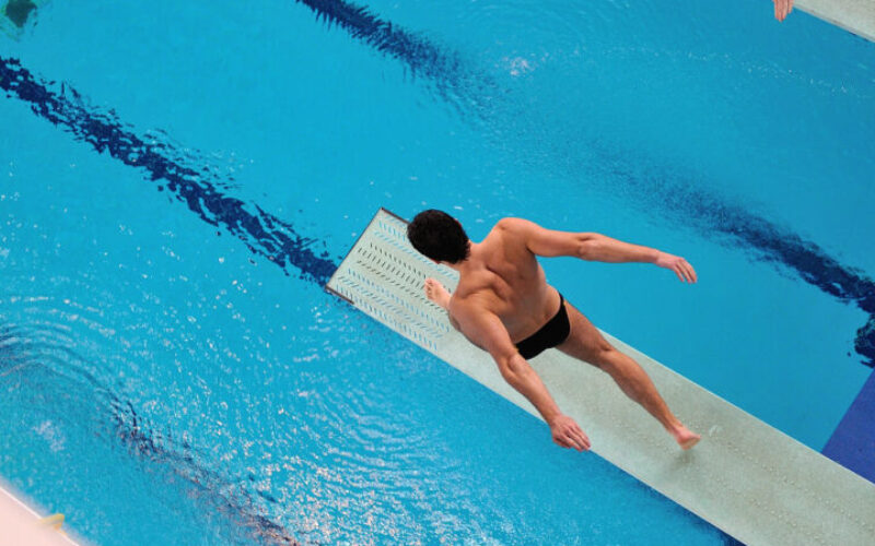 Bild av manlig elev som gör sid redo att hoppa från en trampolin ned i en simbassäng.